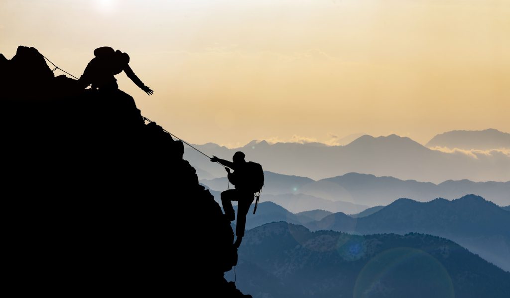 A silhouette of two people climbing a mountain, one with their arm stretched out for the other
